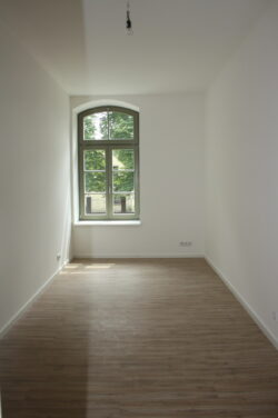 Leerer Raum mit Fenster, Holzboden, weiße Wände.
