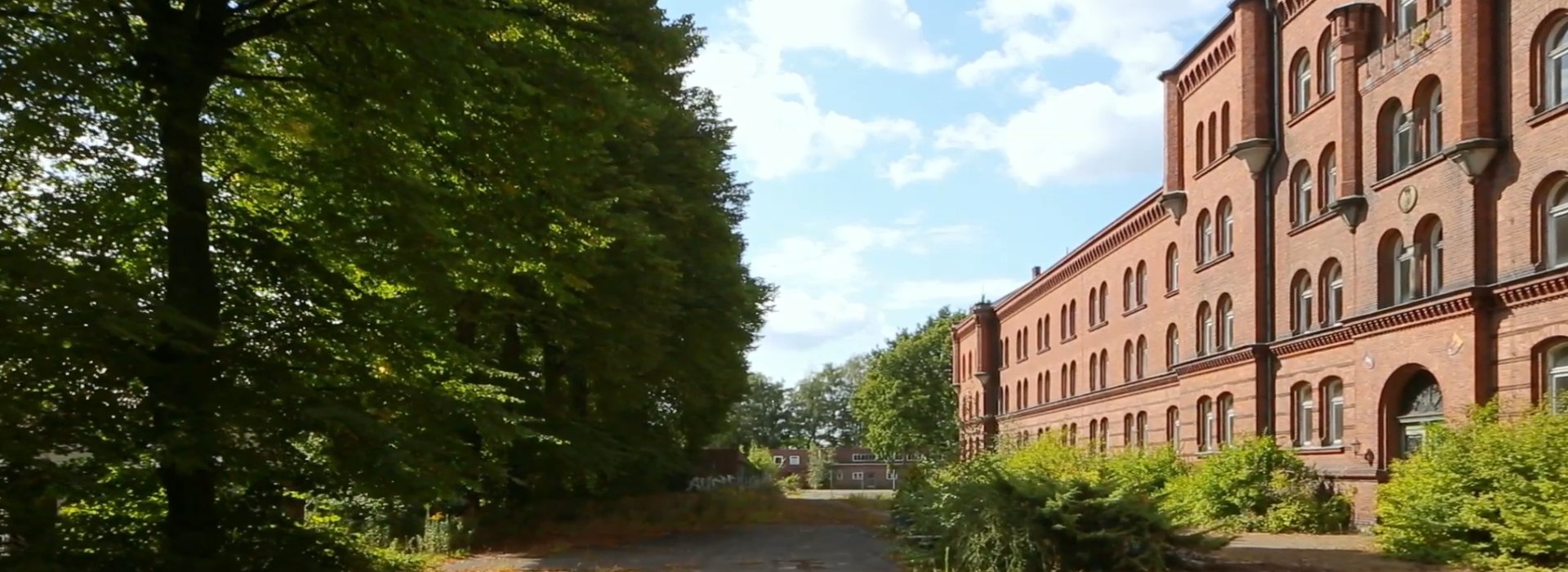 Roter Backsteinbau neben Baumallee unter blauem Himmel.